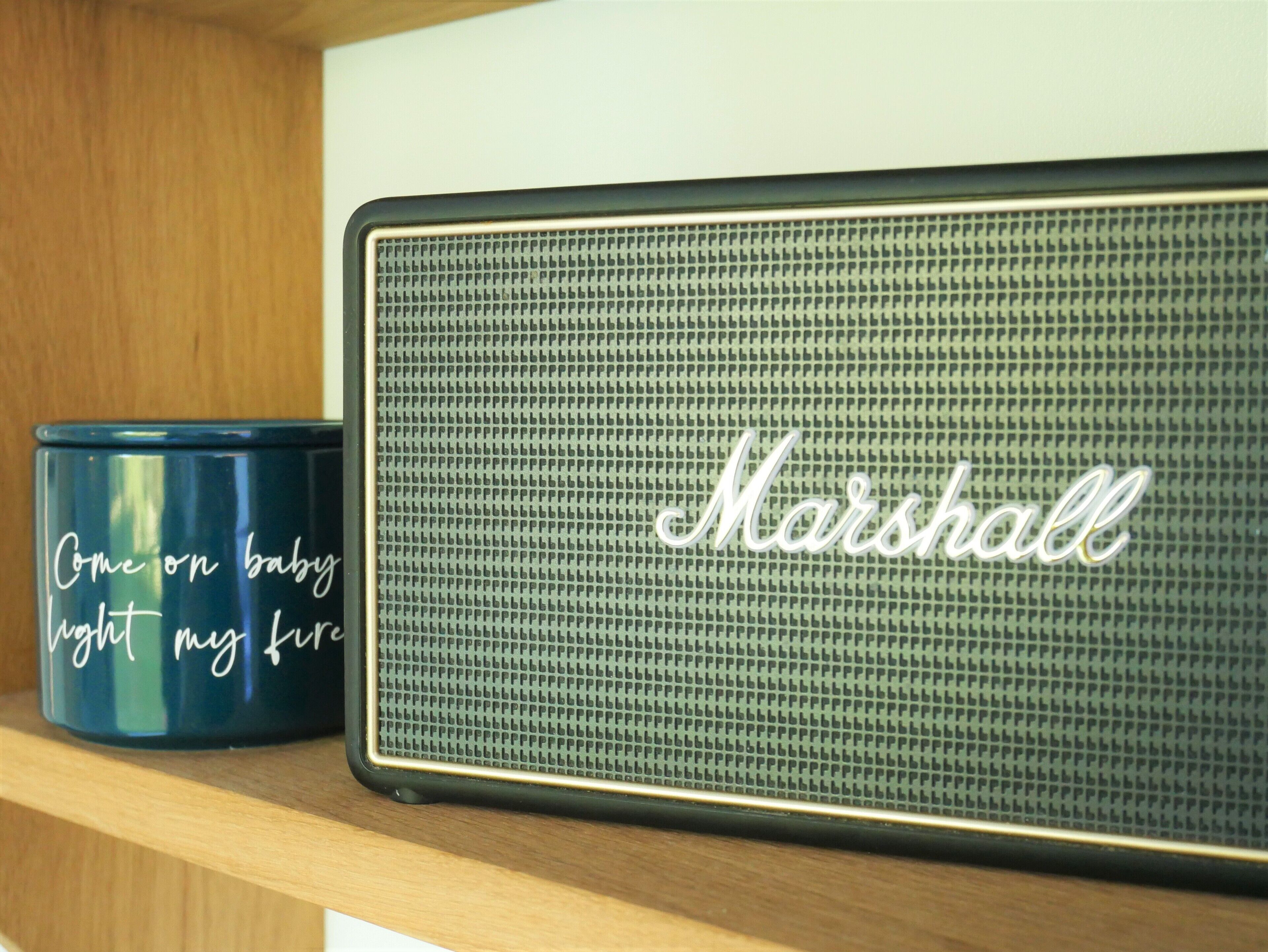 A blue container with the text "Come on baby light my fire" and a Marshall speaker on a shelf.