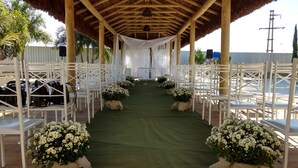Ein Brautgang im Freien mit weißen Stühlen und floralen Dekorationen.