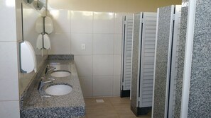 Eine öffentliche Toilette mit drei Waschbecken, einem Spiegel und einem Duschbereich.