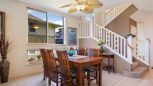 A dining area with a wooden table and chairs, a ceiling fan, and a staircase with white railings.