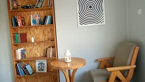 Una estantería de madera llena de libros, un farol blanco sobre una mesita redonda y una silla de madera con cojín.