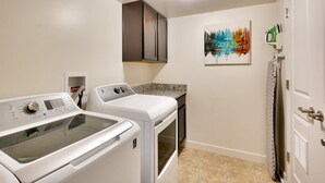 A laundry room with a front-loading washer and dryer, a cabinet above the dryer, a painting on the wall, and a door with a towel rack.