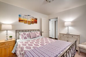 A bedroom with a bed, bedside tables, a lamp, a dresser, and a door leading to another room.