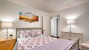 A bedroom with a bed, bedside tables, a dresser, and a chair. There are wall art pieces above the bed and a door leading to another room.