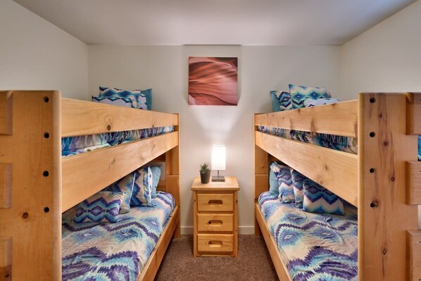 A room with two bunk beds, a small bedside table with a lamp, and a wall-mounted picture.