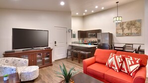 A living room with a flat-screen TV, a red sofa, a coffee table, and a patterned ottoman.