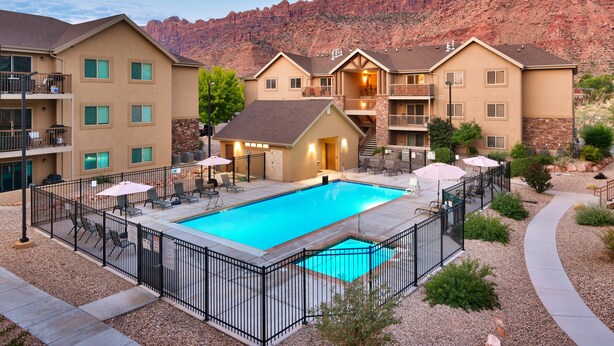 A hotel with a swimming pool, outdoor seating, and a view of red rock formations. - 5G Perfect Moab RedCliff Condo, POOL AND HOT TUB (Moab)