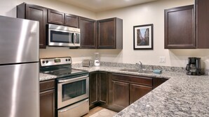A kitchen with dark wooden cabinets, stainless steel appliances, a granite countertop, and a framed picture on the wall. - 5G Perfect Moab RedCliff Condo, POOL AND HOT TUB (Moab)