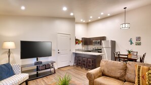Uma sala de estar moderna com um sofá, uma mesa de centro com uma planta, uma TV e uma área de cozinha com micro-ondas, geladeira e banquetas de bar.