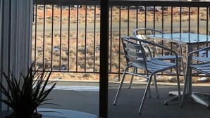 Uma varanda com mesa e cadeiras, com vista para uma paisagem desértica com montanhas ao longe.
