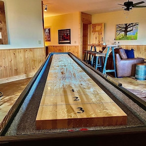 Una mesa de shuffleboard con extremos numerados, paredes de madera y una zona de bar al fondo.