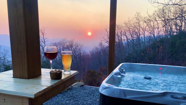 Une table en bois, un jacuzzi et deux verres de boissons, le tout installé devant un magnifique coucher de soleil.