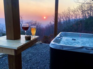 Una mesa de madera con un jacuzzi y dos vasos de bebidas, frente a una vista panorámica al atardecer.