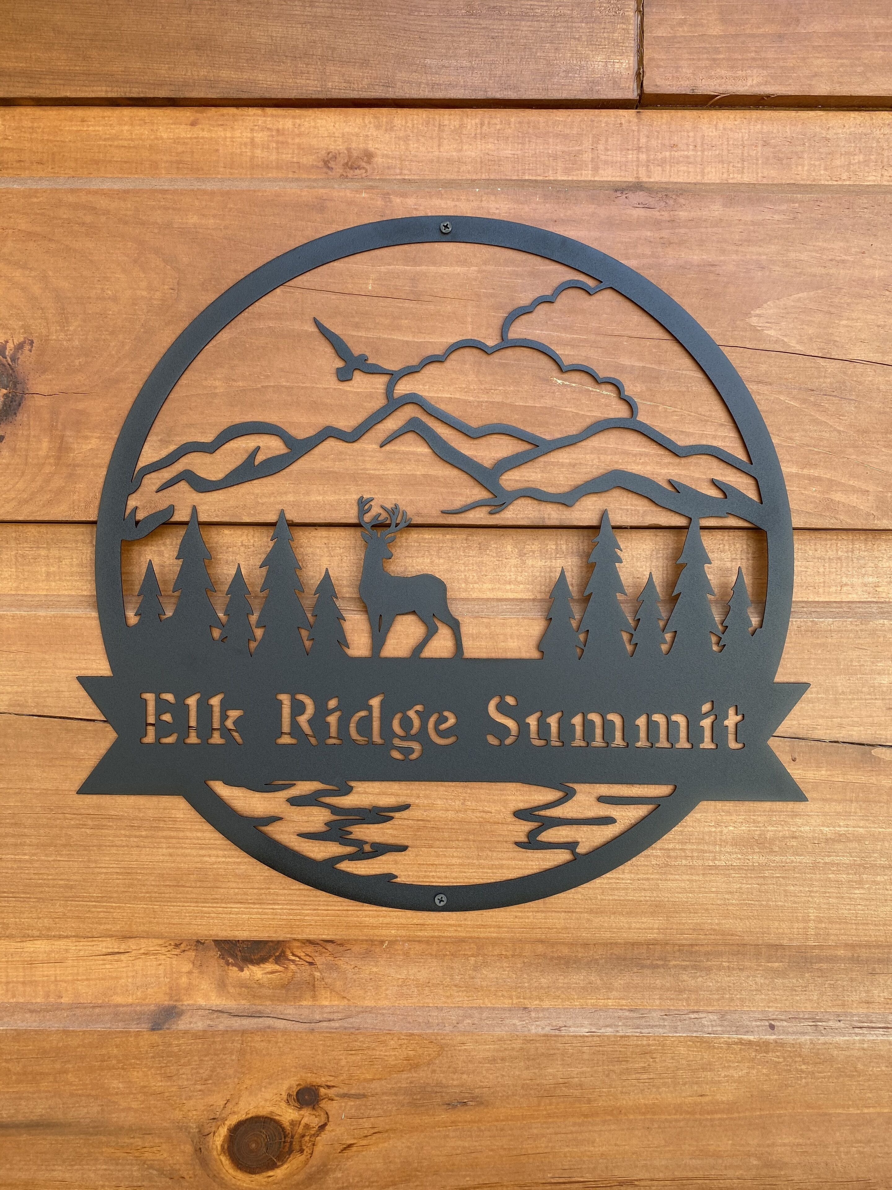 A wooden sign with a silhouette of a deer, trees, and mountains, and the text "Elk Ridge Summit".