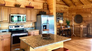 Une cuisine rustique, située dans une cabane en bois, avec des comptoirs en granit, un four à micro-ondes, un réfrigérateur et des armoires en bois.