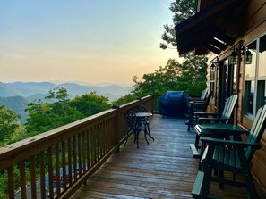 A wooden deck with outdoor seating and a barbecue grill, overlooking a mountainous landscape.