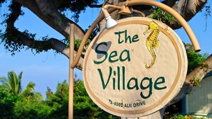 Puinen kyltti, jossa lukee ”The Sea Village” ja on kuvattuna meritähti, on kiinnitetty puuhun.