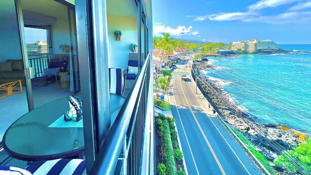 Un balcón con vista a una carretera costera, un comedor y un hotel al fondo.