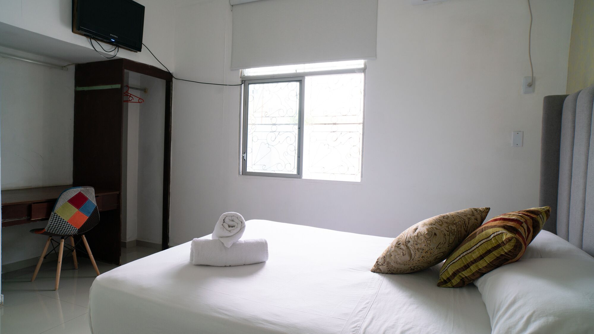 Ein Hotelzimmer mit Bett, Schreibtisch, Stuhl, Fenster und einem Fernseher an der Wand.