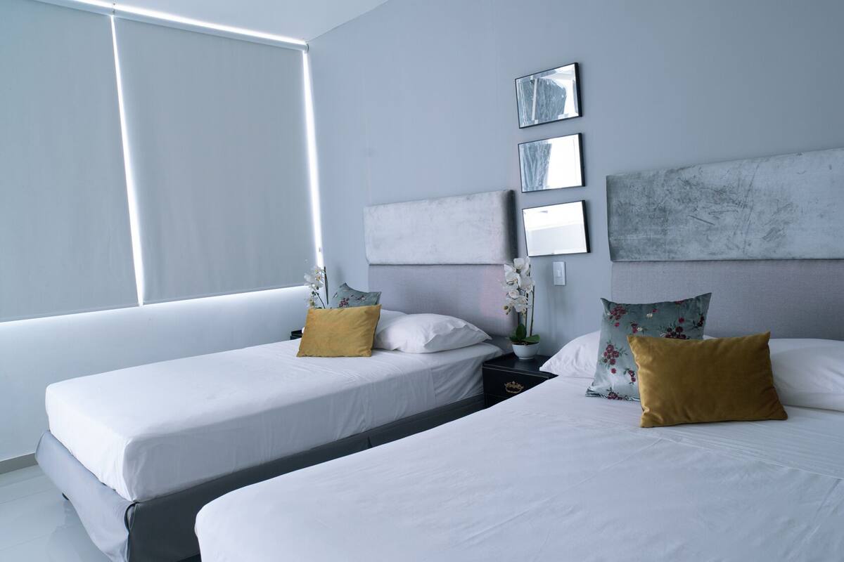 A hotel room with two beds, white bedding, and a large window providing natural light.