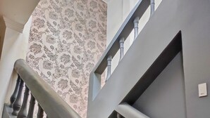 A staircase with a grey railing and wooden steps, leading to a landing with a patterned wallpaper and a chandelier. - Hotel Boutique Casa Umiña (Manta)