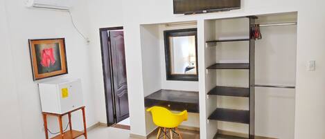 Una habitación con una televisión montada en la pared, un cuadro enmarcado, un sillón amarillo y una unidad de estanterías empotrada.