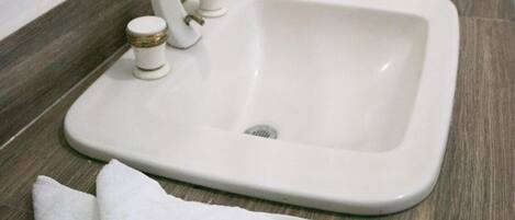 Un baño con un lavamanos blanco, un espejo y una orquídea en maceta.
