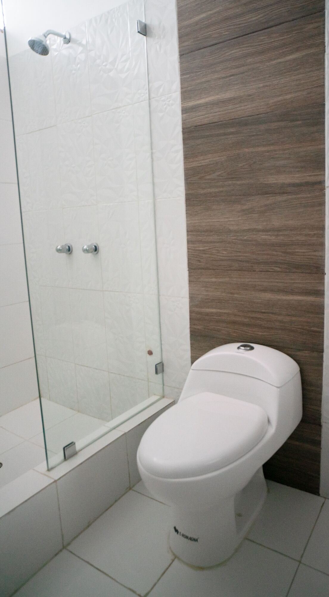 Een badkamer met een douchecabine van glas, een wit toilet en een wand van hout.
