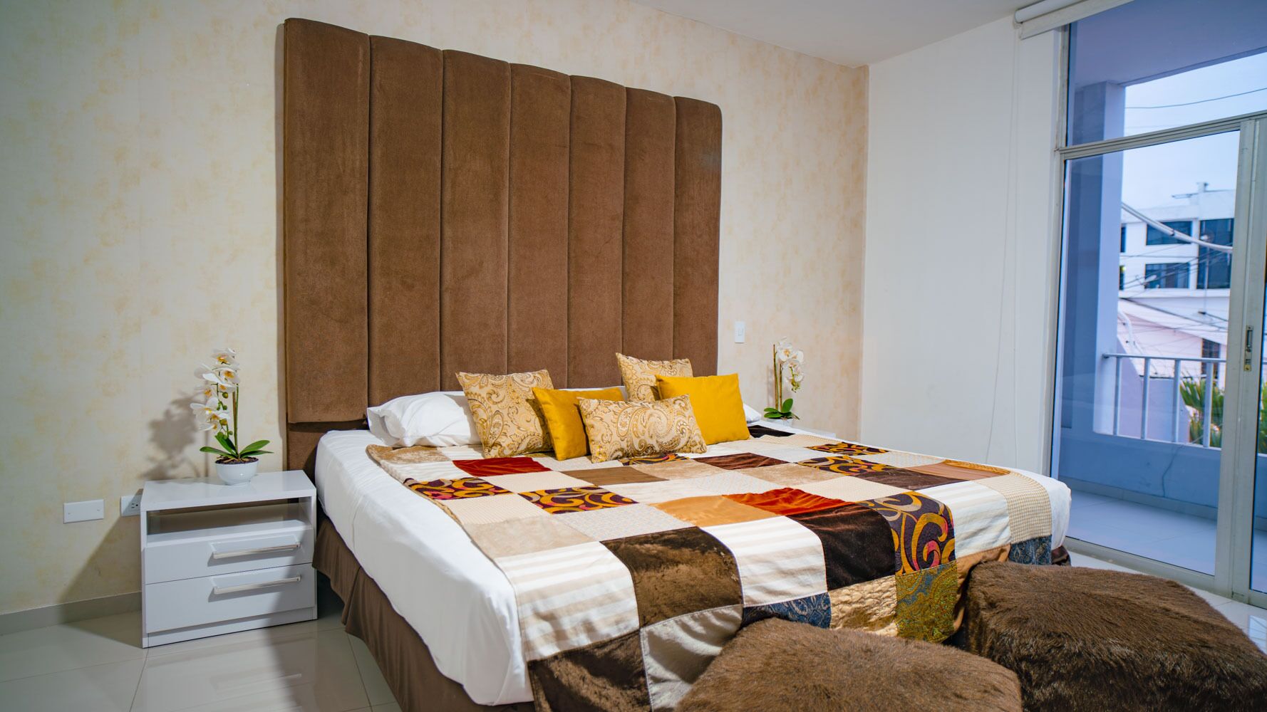 Un dormitorio moderno con una cama grande, una mesita de noche, una planta en maceta y vistas al exterior a través de un ventanal.