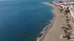 Eine Luftaufnahme einer Küstenregion mit einem Sandstrand, blauem Meer und einer Reihe von Gebäuden entlang der Küste.