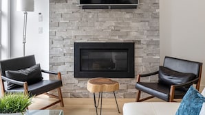 Un salon moderne avec un mur en pierre, un téléviseur à écran plat, une cheminée et deux fauteuils en cuir.