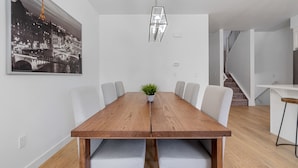 Un coin repas avec une table en bois, des chaises à revêtement gris, une plante en pot et un luminaire suspendu.