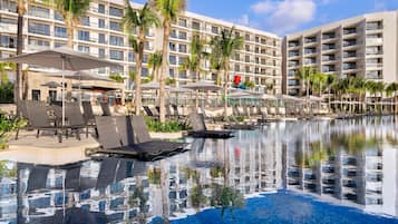 A hotel pool area with lounge chairs, umbrellas, and palm trees.