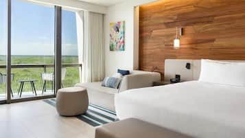 A modern hotel room with a large bed, a sofa, a dining area with chairs, a wooden accent wall, and a painting.
