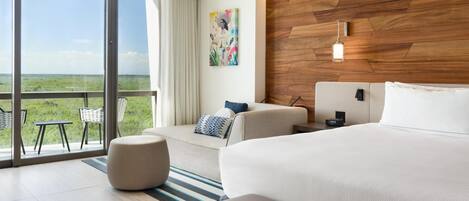 A modern hotel room with a large bed, a sofa, a dining area with chairs, a wooden accent wall, and a painting.