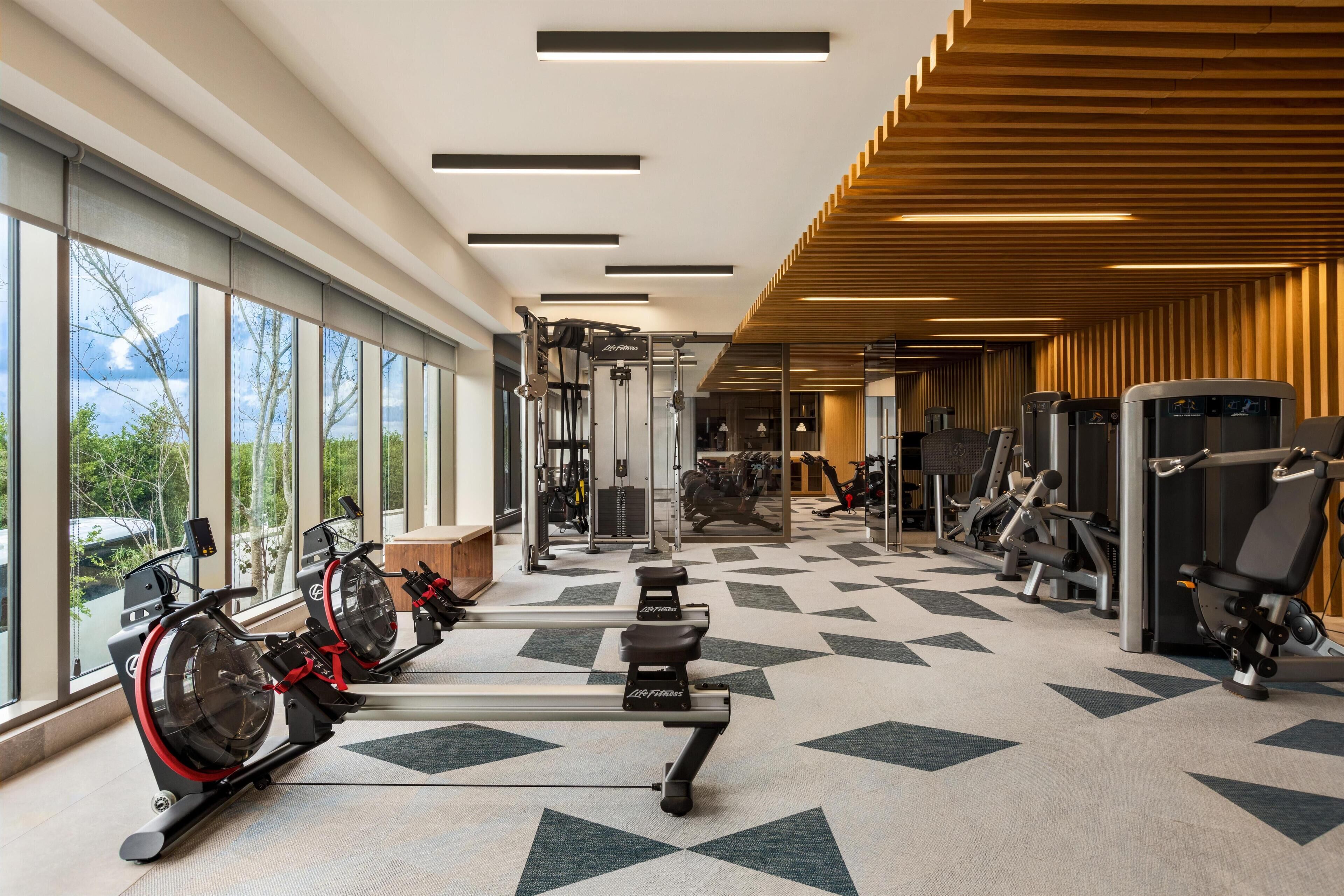 Une salle de sport équipée de machines de cardio, de matériel de musculation et de grandes fenêtres donnant sur l’extérieur.
