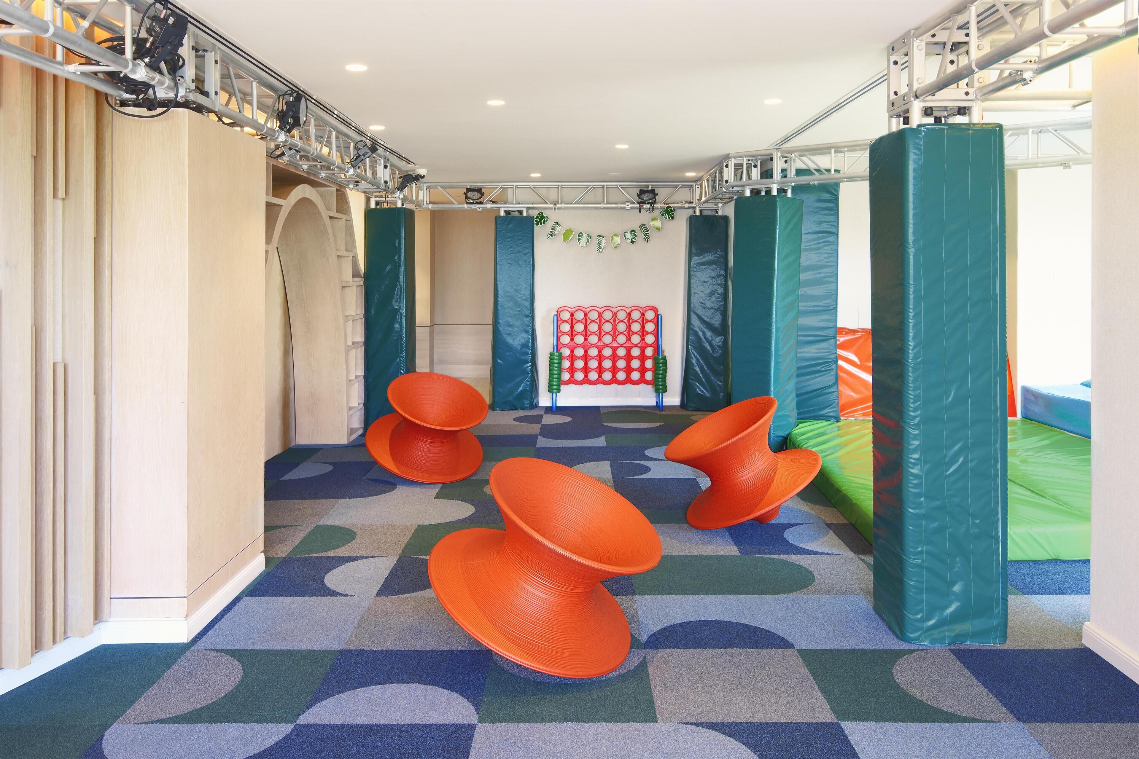 A playroom with colorful padded play structures, a red playhouse, and a patterned carpet.