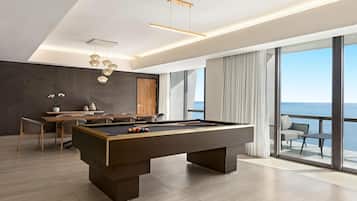 A modern pool table in a spacious room with a dining area, large windows, and a view of the sea.
