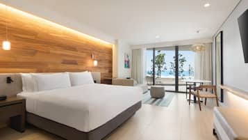 A modern hotel room with a large bed, a wooden accent wall, a balcony with a view, and a dining area with a table and chairs.