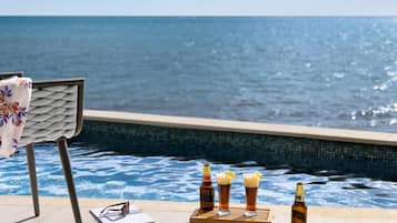 A poolside setting with a chair, a notebook, and three glasses of beer and a bottle on a tray.