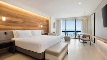 A modern hotel room with a large bed, a desk, and a view of the ocean.