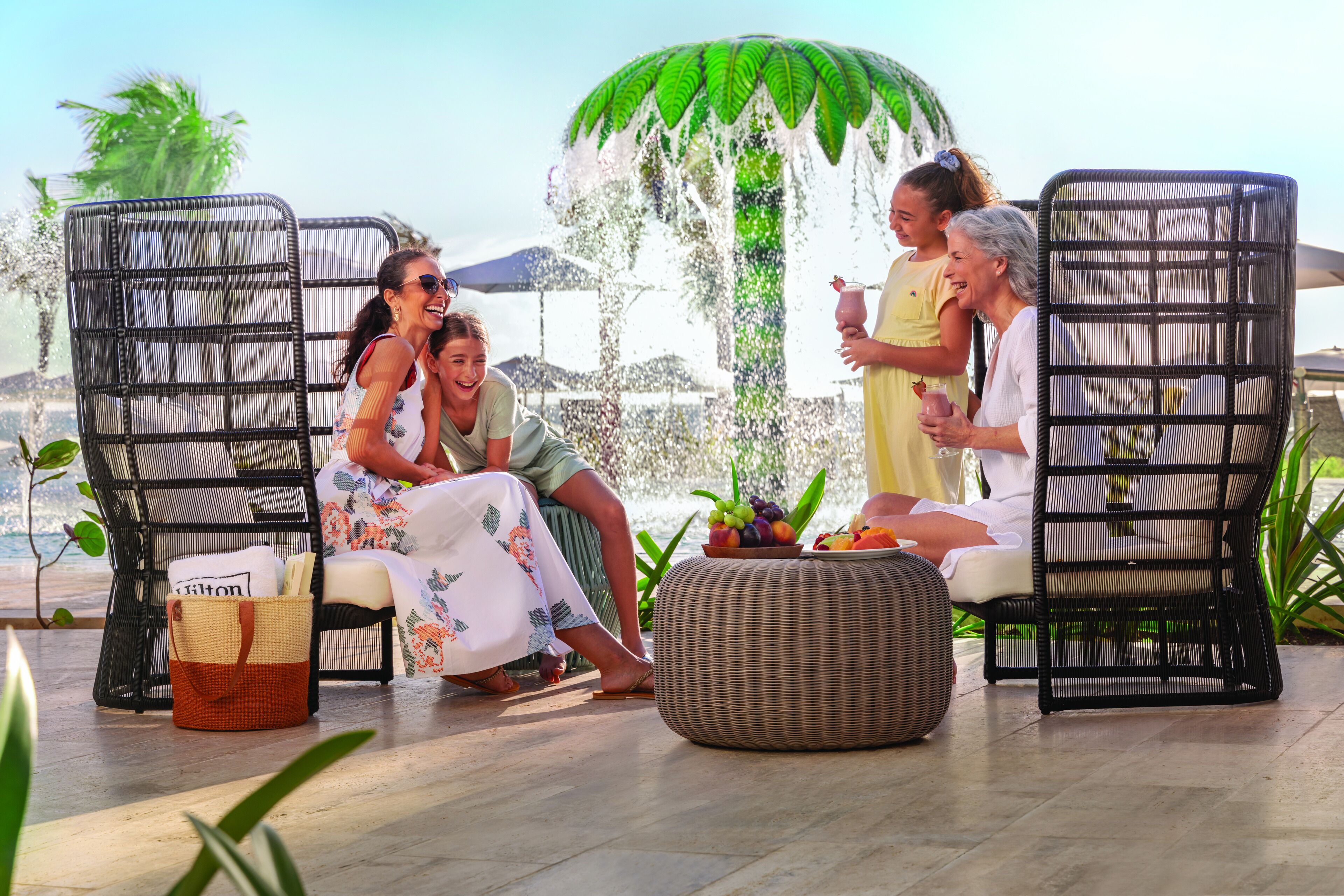Un groupe de personnes est assis sur des fauteuils de jardin, avec un pouf en osier et un panier placés au premier plan.