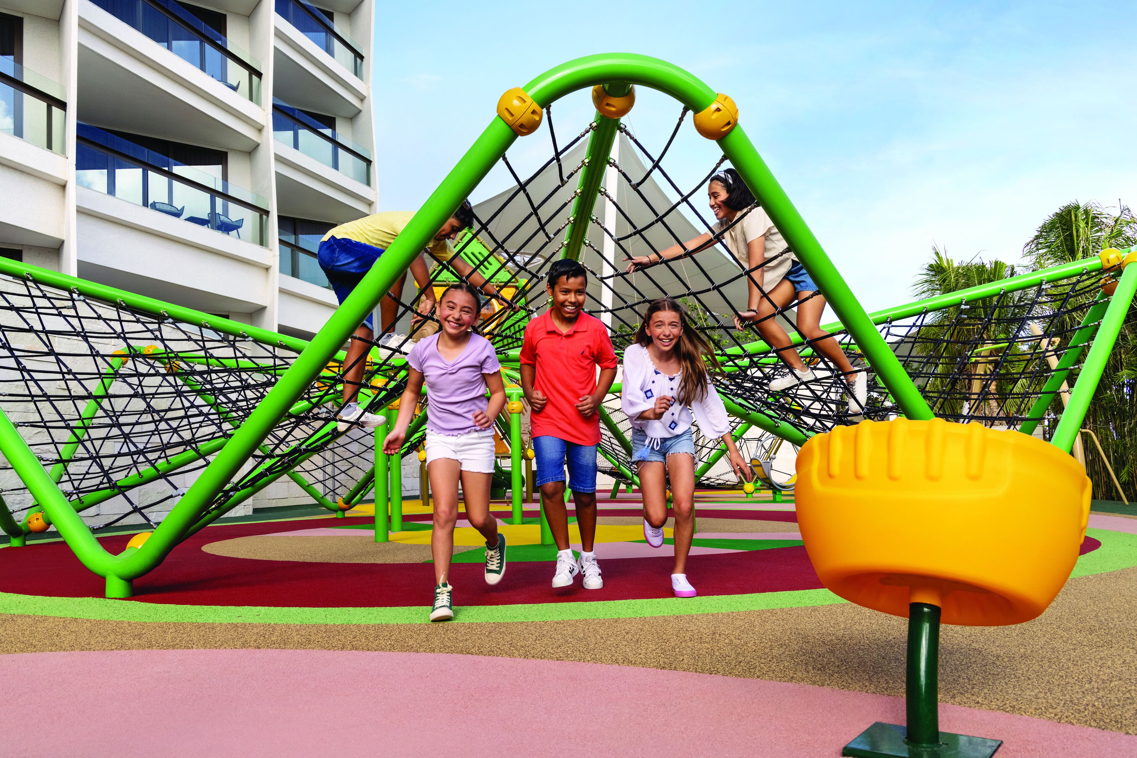 Een speeltuin met een klimstructuur met net en een geel speelgedeelte op de voorgrond.