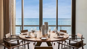 A dining table set for six with a view of the sea through large windows.