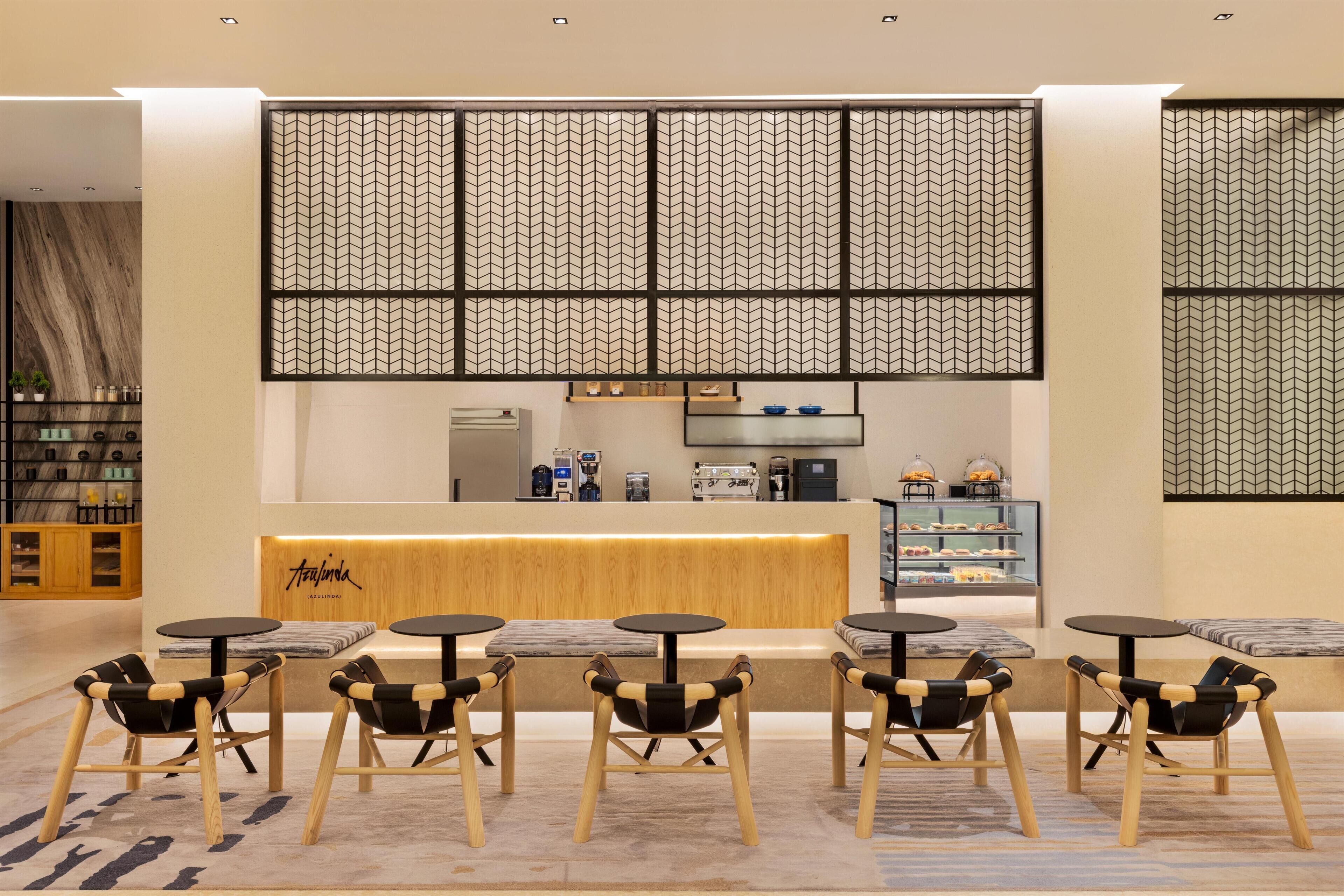 A modern cafe with a wooden counter, black and wooden chairs, and a patterned wall.