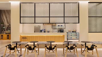 A modern cafe with a wooden counter, black and wooden chairs, and a patterned wall.