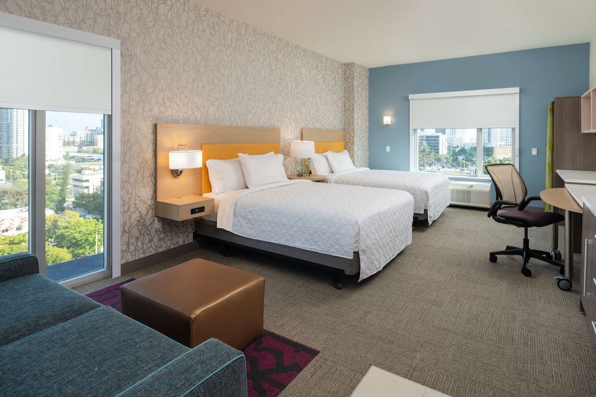 Ein Hotelzimmer mit zwei Betten, einem Schreibtisch, einem Stuhl und einer Couch.