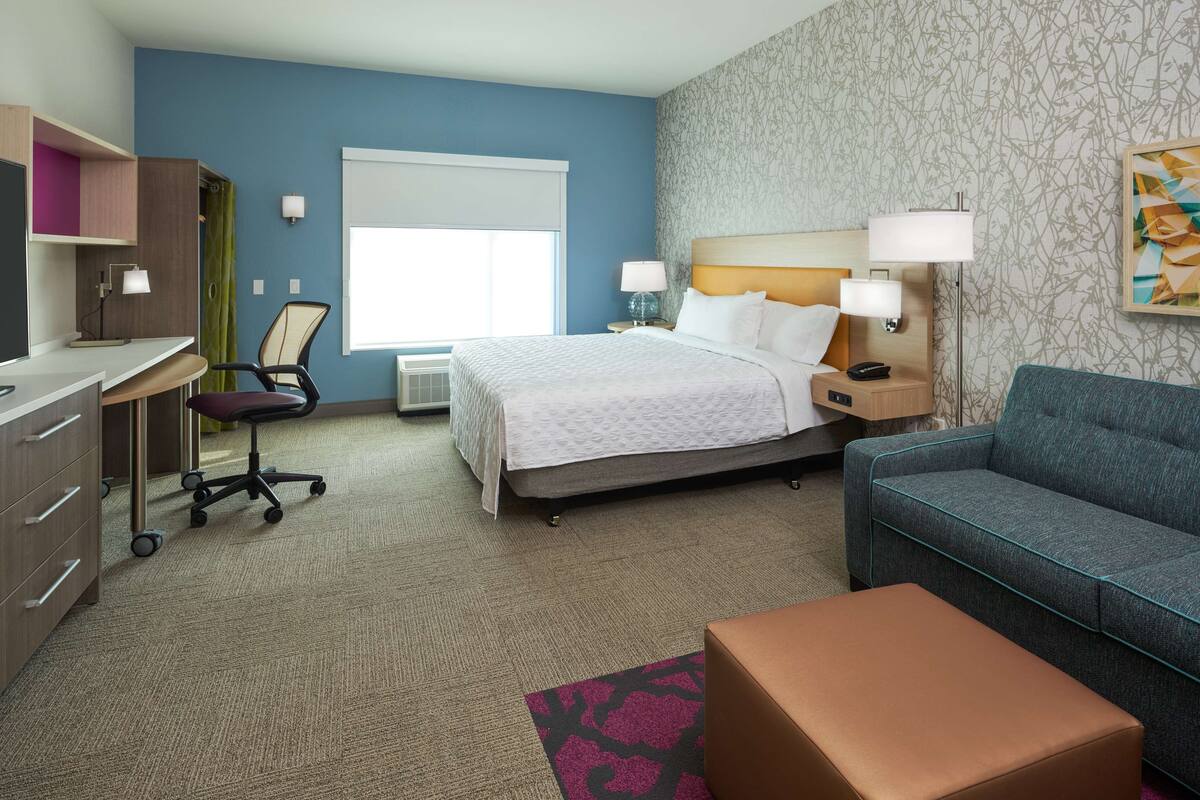 Ein Hotelzimmer mit Bett, Schreibtisch, Stuhl, Sofa und kleinem Tisch.
