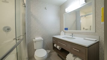 Un baño moderno con cabina de ducha de vidrio, inodoro, lavabo con espejo y tocador con toallas.