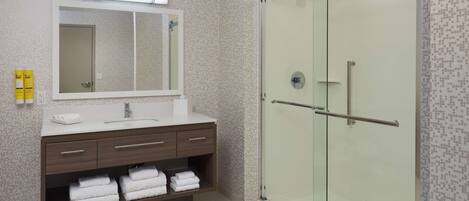 A modern bathroom with a glass-enclosed shower, a vanity with a mirror, and neatly folded towels.